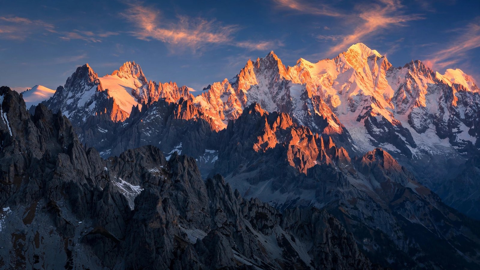 Snow-capped alpine peaks glowing orange-pink in golden hour light