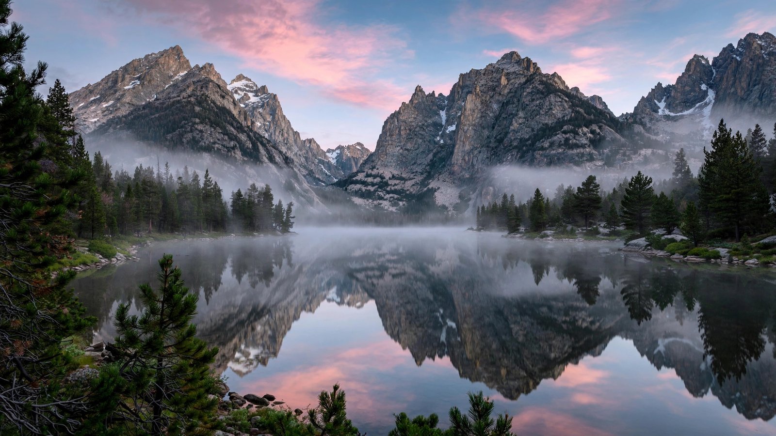 Mountain lake reflecting granite peaks at dawn with morning mist